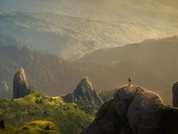 Photo of a Vast Landscape with a Person on top of a Boulder